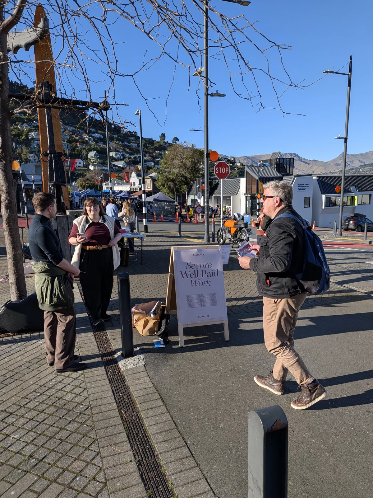 People sharing Alliance leaflets beside a campaign sign in Lyttelton