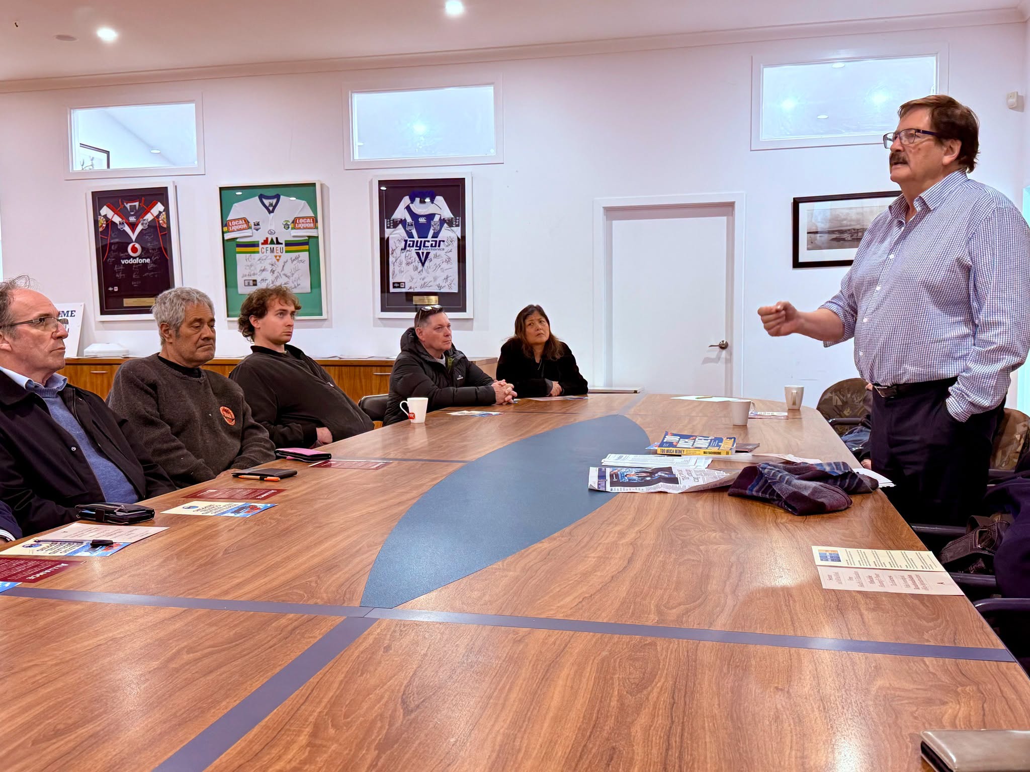 A speaker addresses attendees seated around a table at an Alliance Party meeting