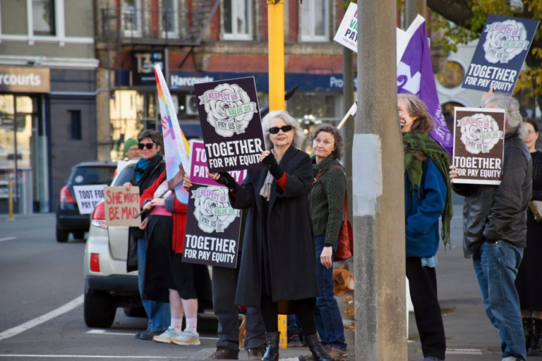 People holding Together for Pay Equity signs at a street demonstration.