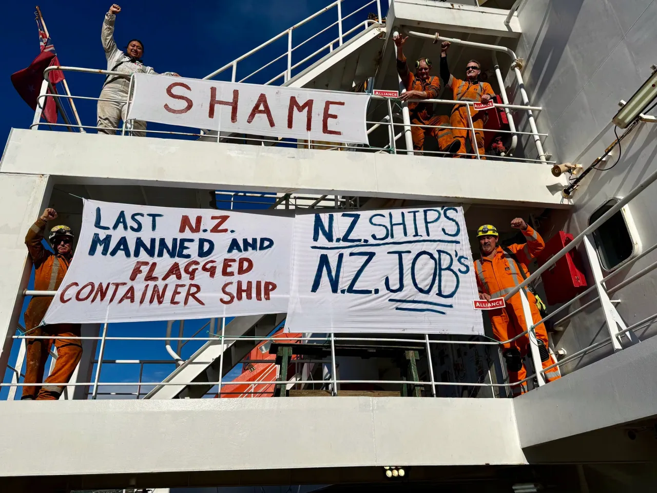 Maritime workers aboard a ship with banners calling for New Zealand ships and jobs.