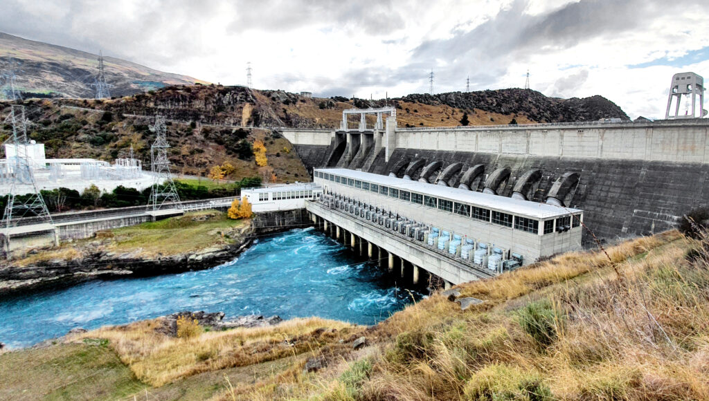 Roxburgh Dam and hydroelectric powerhouse in Otago, with transmission pylons and water flowing into the Clutha River.